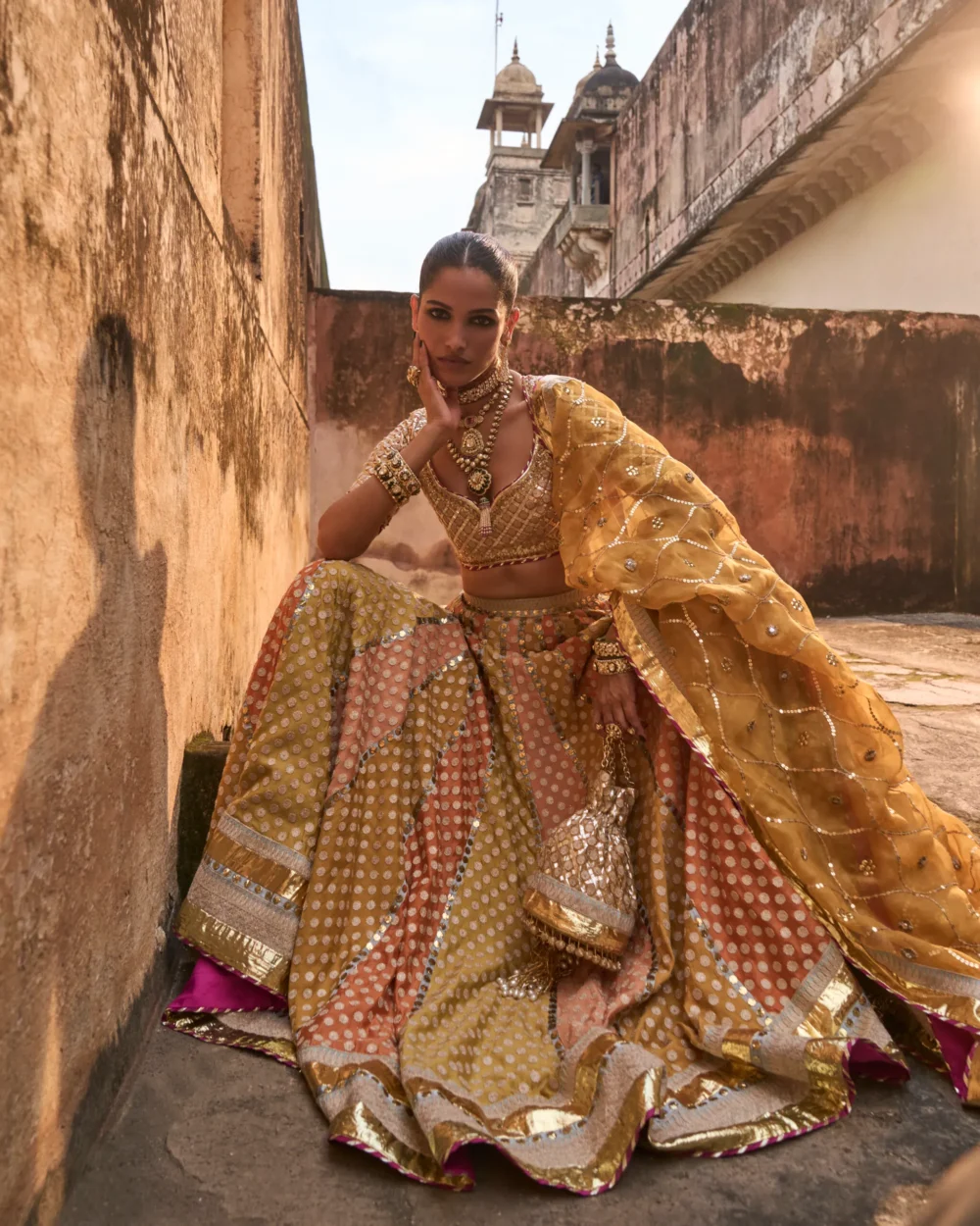 Khaddi Silk Lehenga Set featuring an orange blouse with gota work, a mustard lehenga with ari work panels, and a mustard organza dupatta.